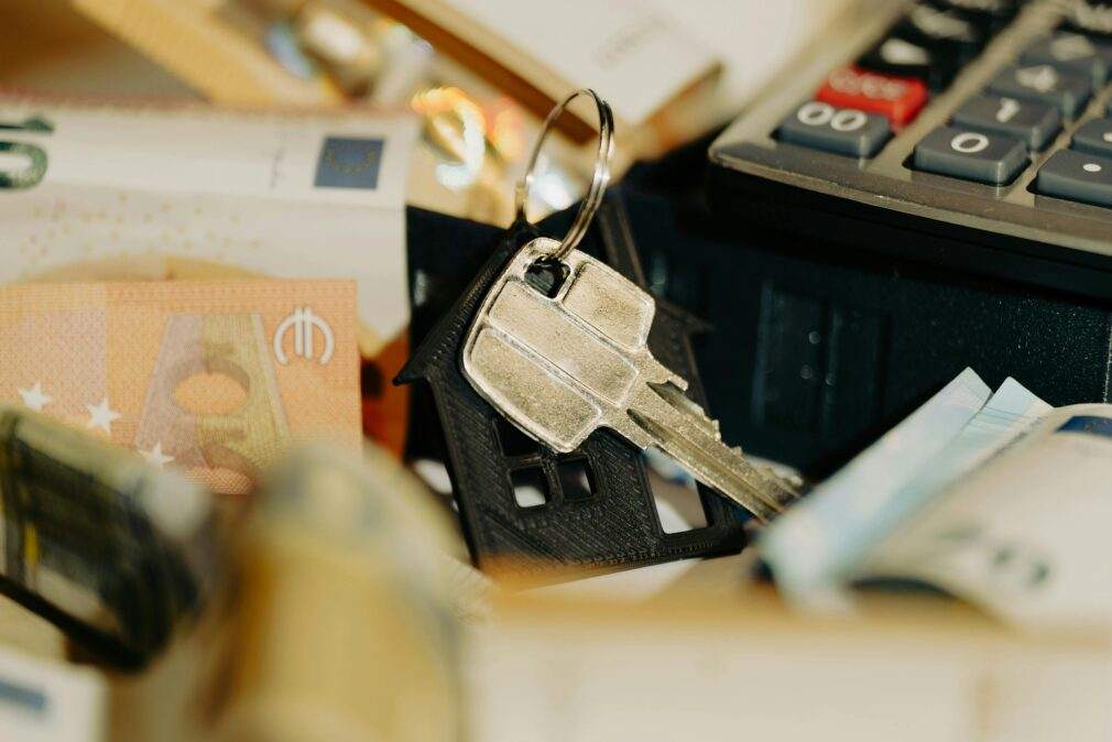 House keys rest on a keychain with euro banknotes and calculator, symbolizing real estate investment.