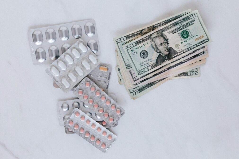 Blister packs of pills and US dollars on a white surface.