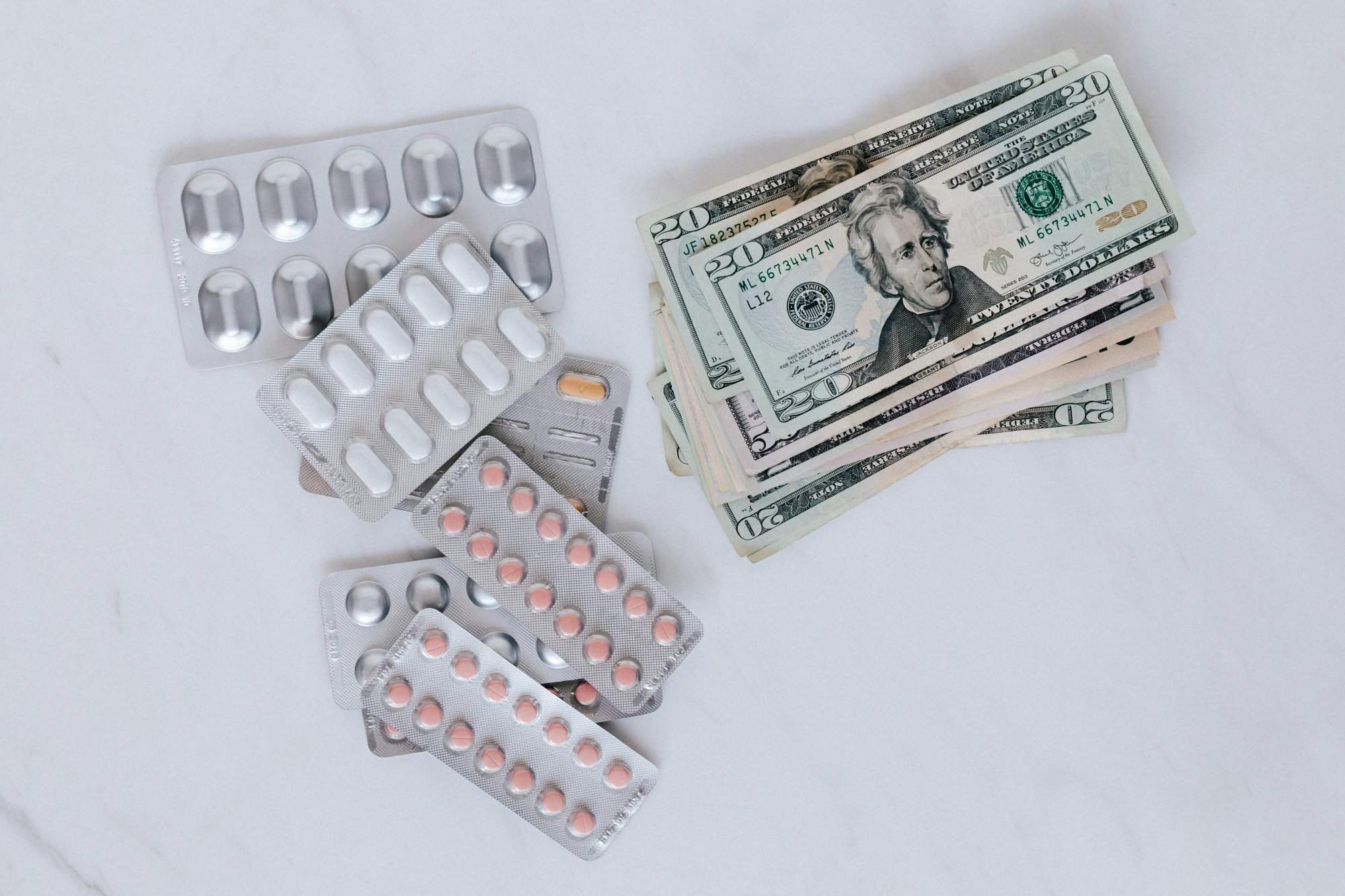Blister packs of pills and US dollars on a white surface.