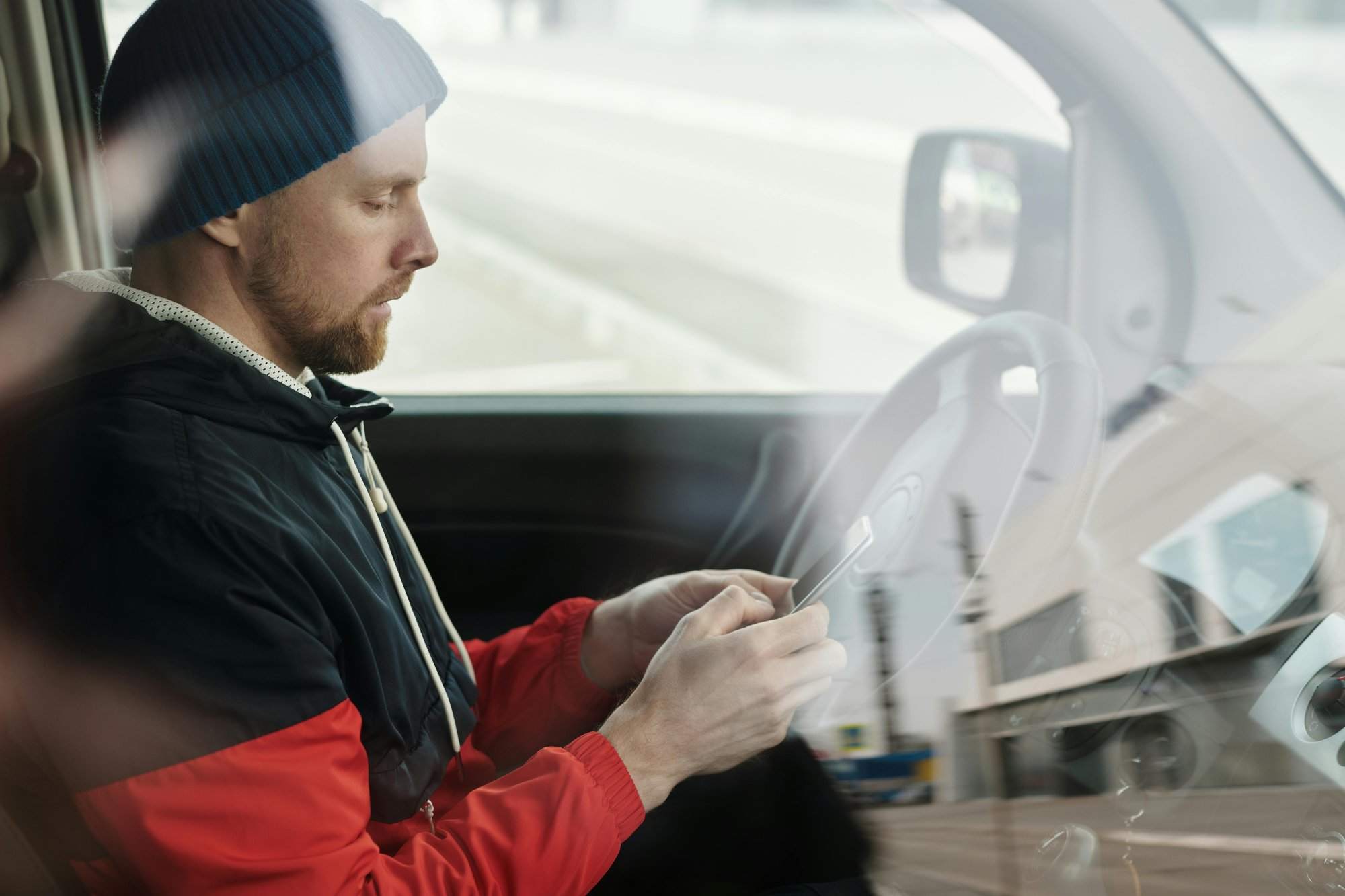 Man sitting in a car using a smartphone, reflecting urban lifestyle. Side view.