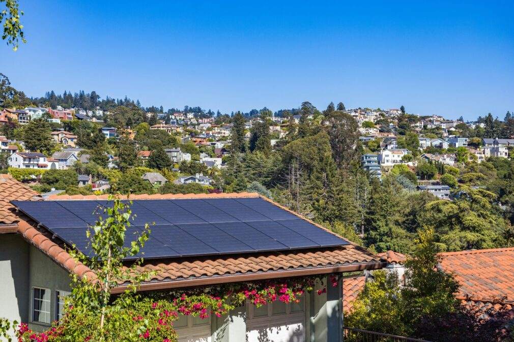 Solar panels on a suburban home, surrounded by lush greenery and a sunny blue sky.