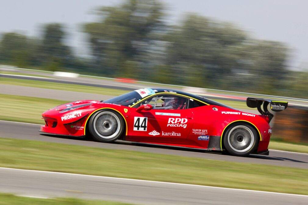 High-speed red race car in motion on track, captured in vibrant daylight.