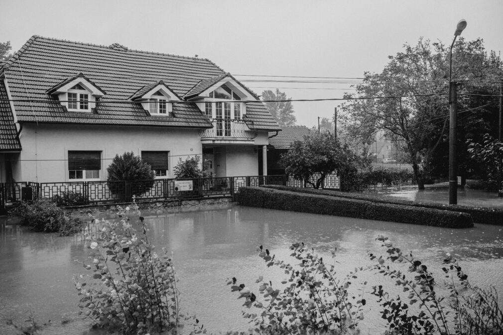Black and white image of a flooded home surrounded by rising water.