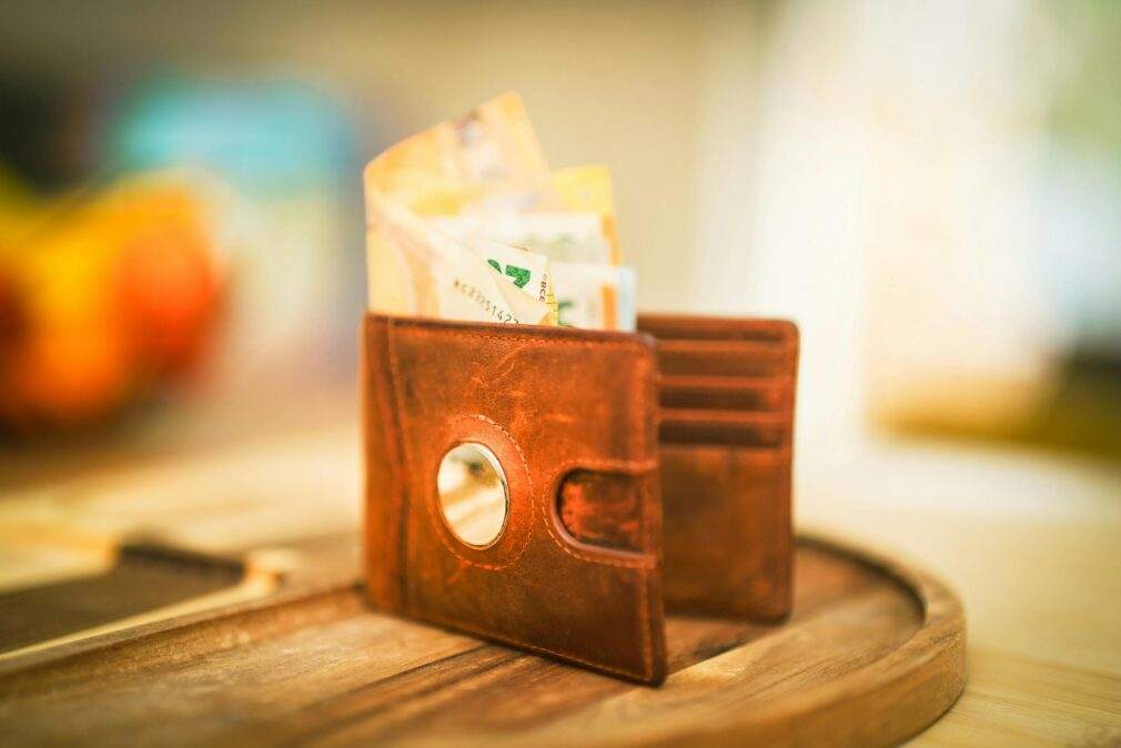 A brown leather wallet filled with various currencies sitting on a wooden table, symbolizing financial savings.