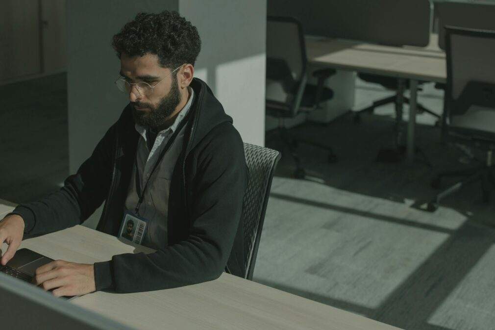 Bearded man working on a computer indoors, focused on cybersecurity tasks.