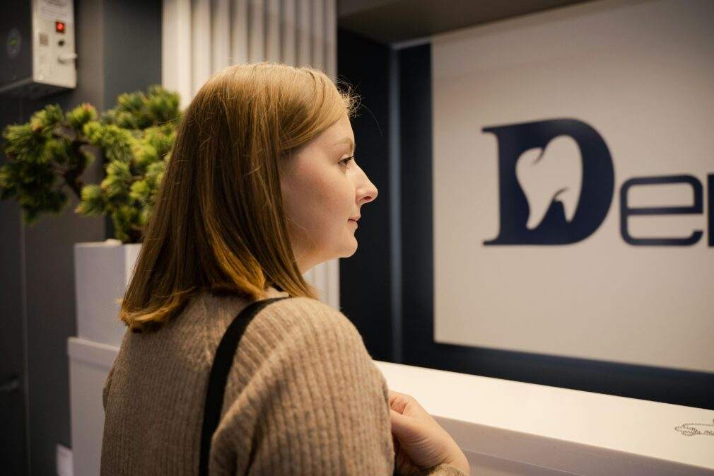 A woman waiting at the dental clinic reception, viewed from the side. Indoor setting.