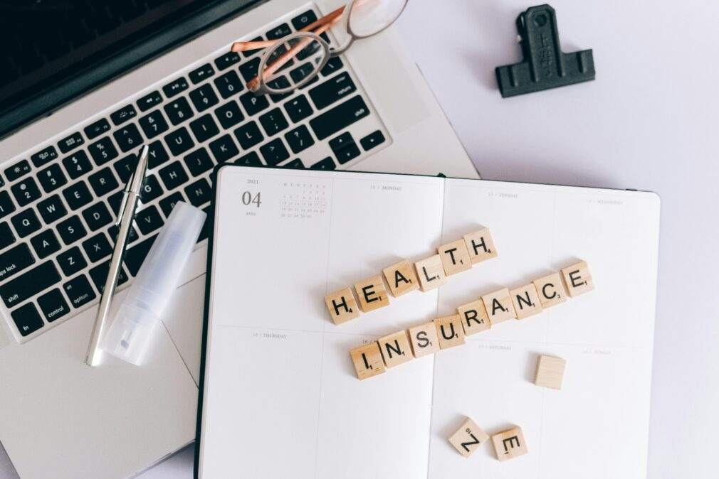 Scrabble tiles spelling health insurance on a planner next to a laptop.