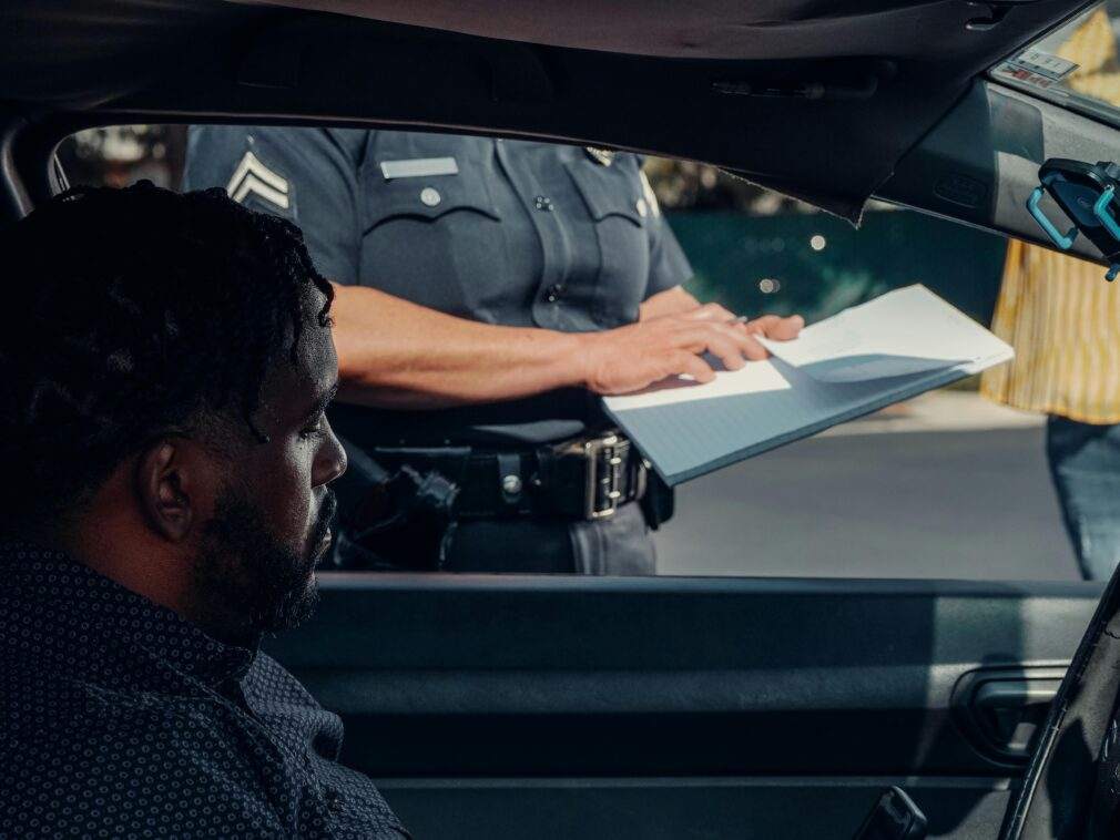 A police officer issues a traffic ticket to a man in a car. Close-up view of the interaction through the window.