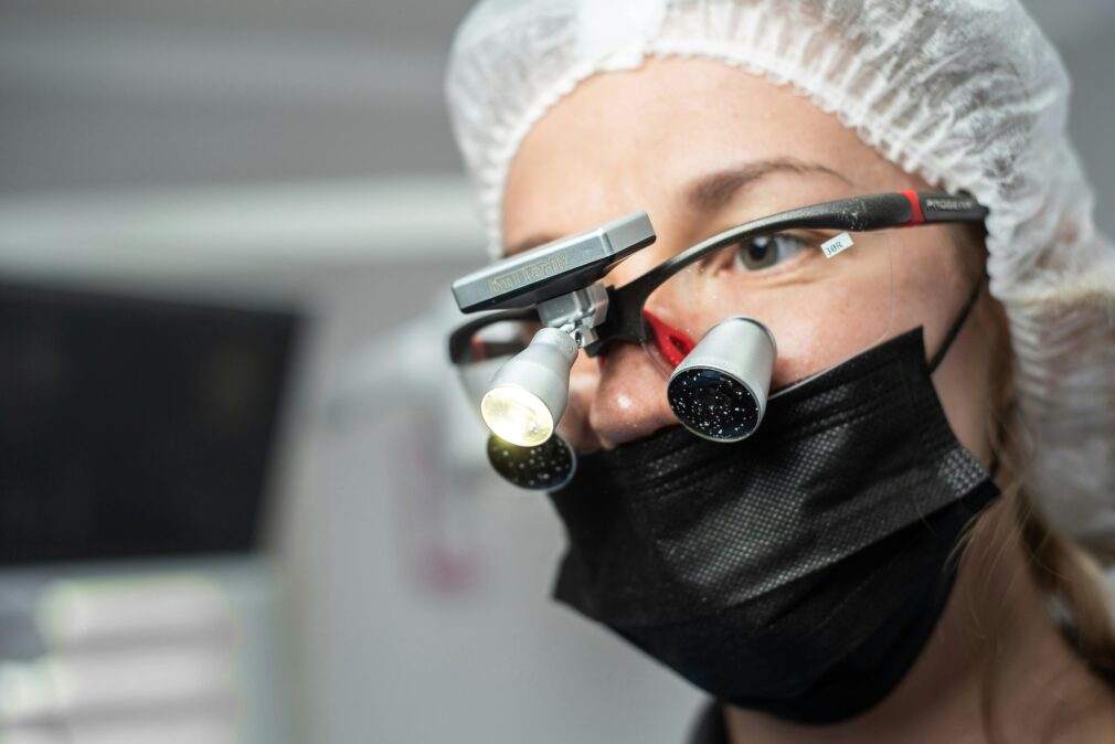 Female dentist wearing dental loupes and face mask, focused on patient care.