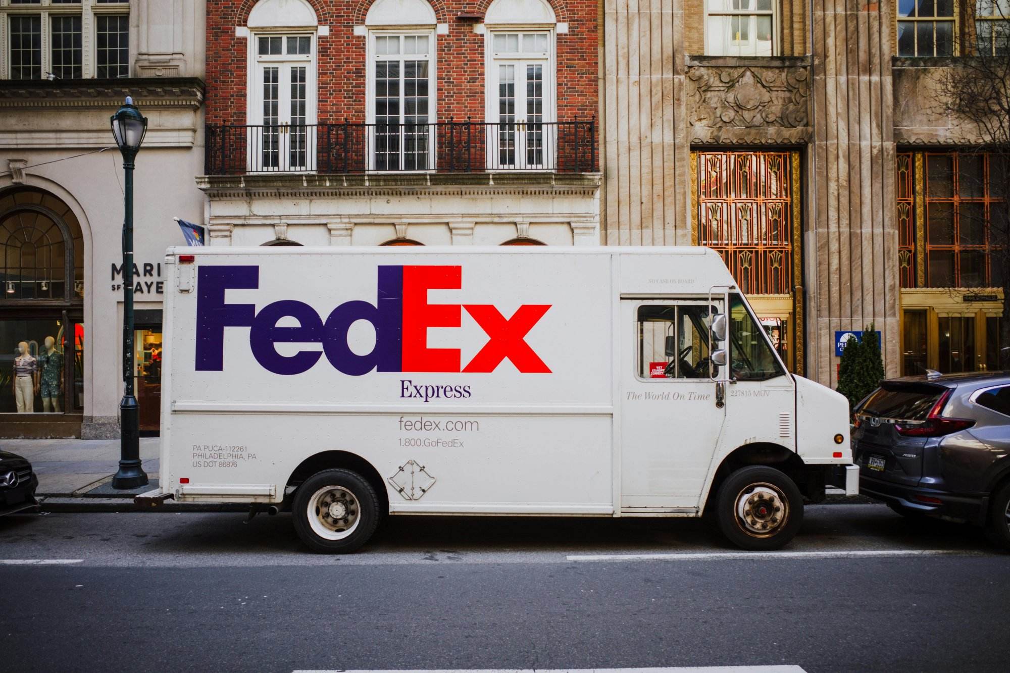 FedEx delivery truck parked on busy city street next to urban buildings.