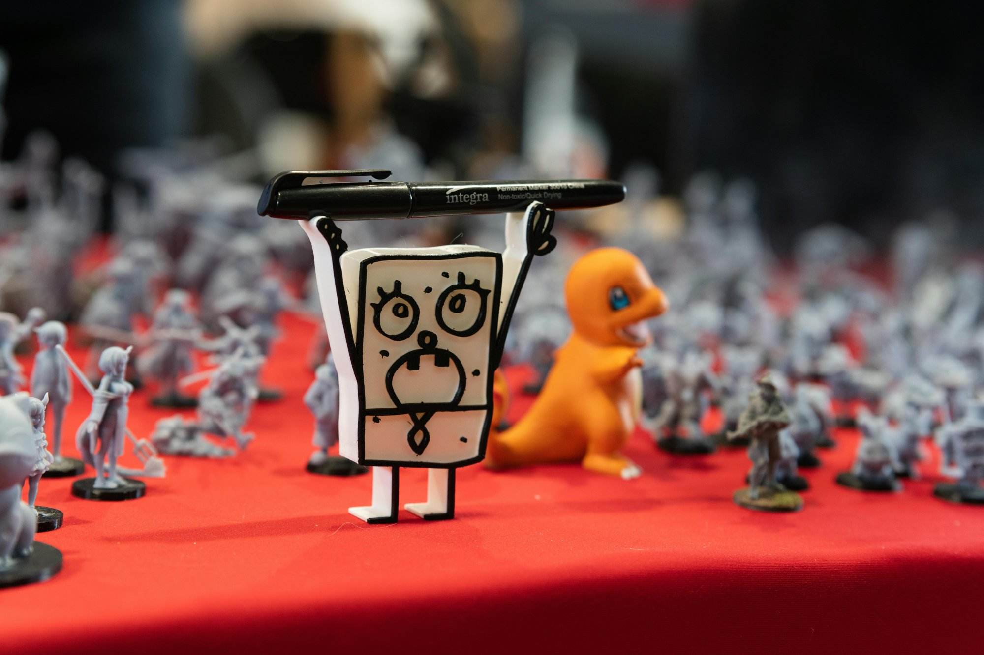 Close-up of assorted figurines and toys displayed on a red table at a convention.