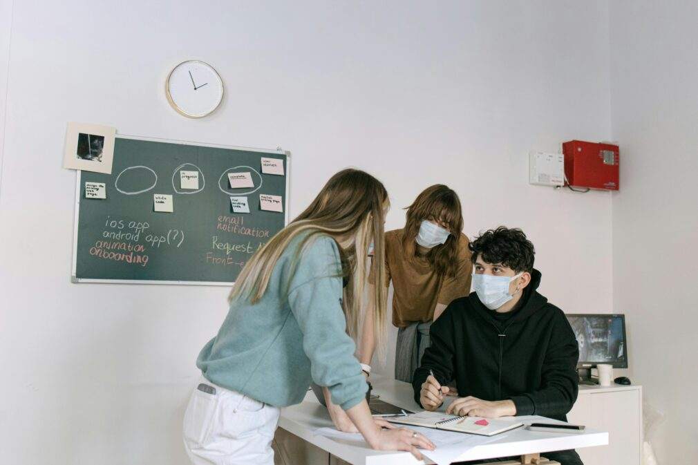 Business team brainstorming ideas on Blackboard while wearing face masks for safety indoors.