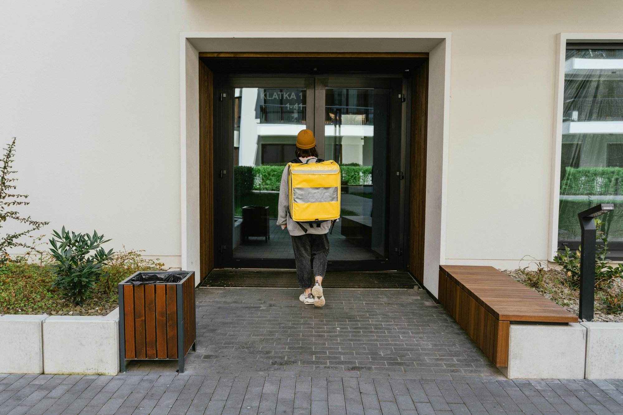 A delivery person with a yellow thermal bag approaches a customer's door in a city setting.