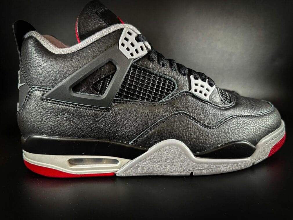 Close-up of a black leather sports shoe with red sole detailing against a black backdrop.