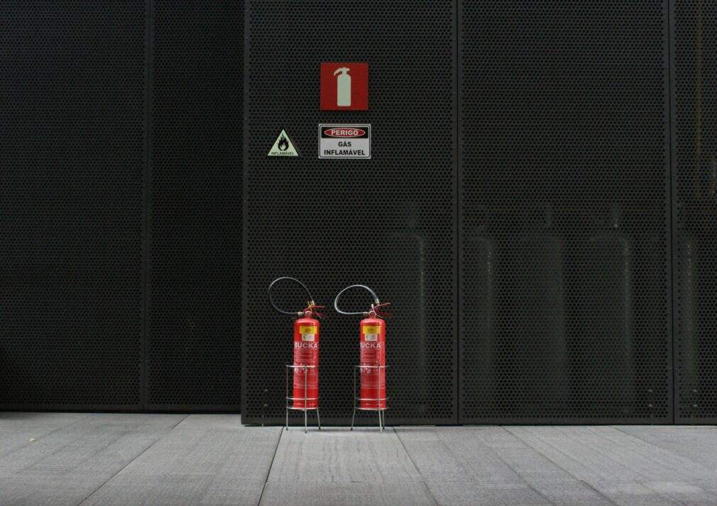 Red fire extinguishers against industrial metal wall with warning signs.