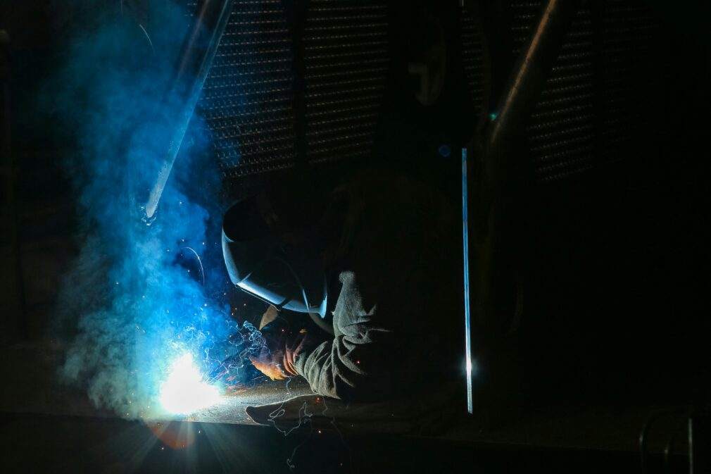 A skilled welder wearing protective gear works on metal, emitting bright sparks and smoke.