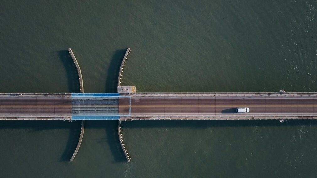 Top-down aerial shot of a bridge crossing over water with a white car driving.