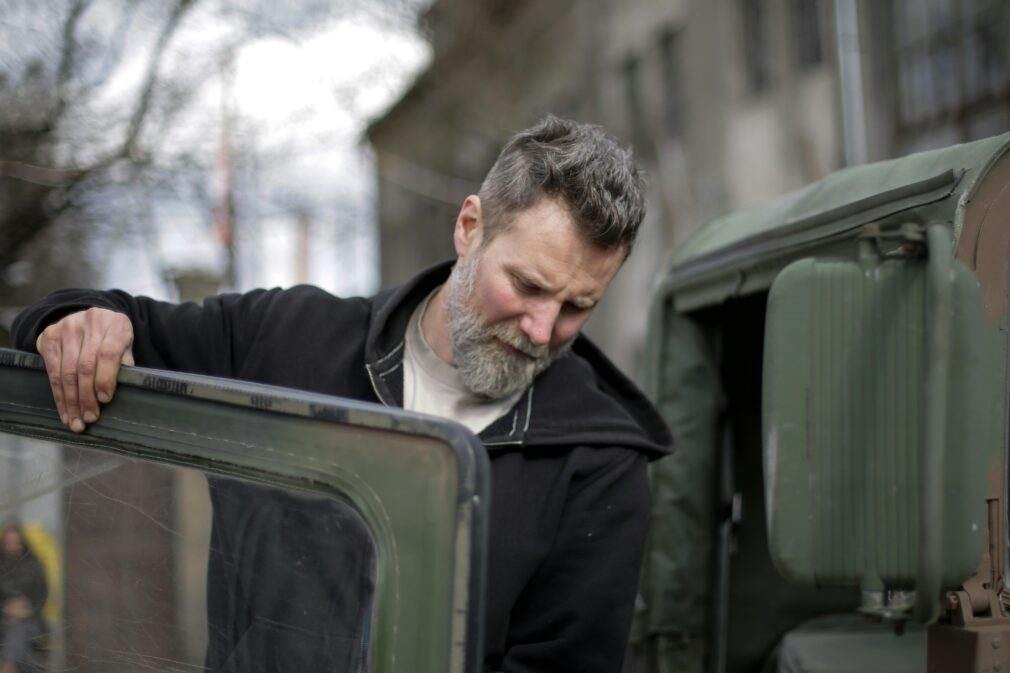 Mechanic inspects a military vehicle door outside, showcasing expertise and focus.