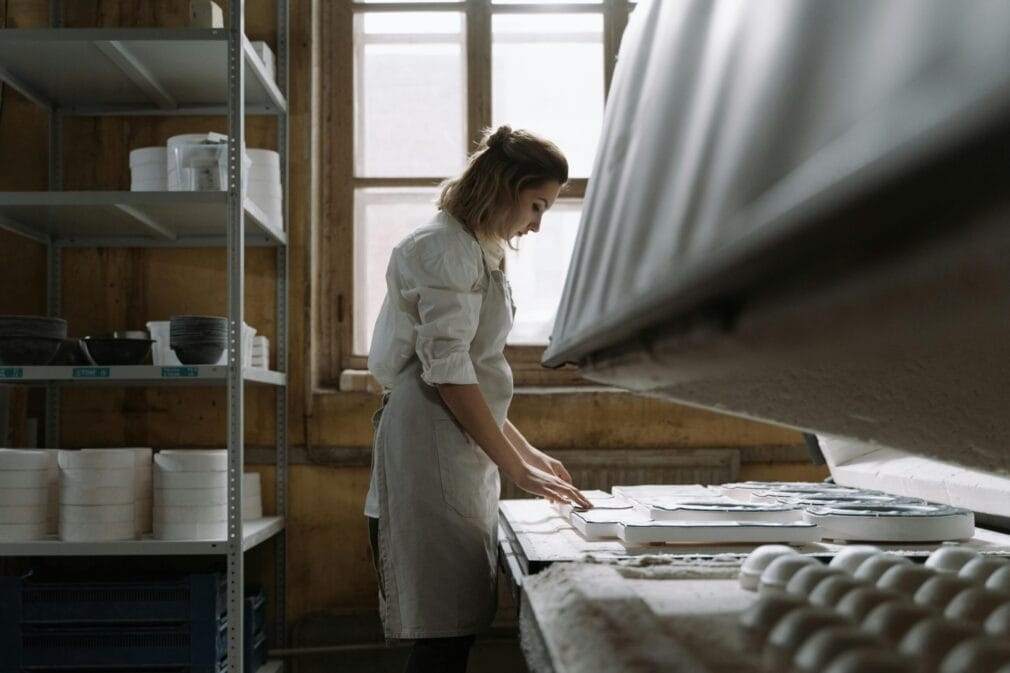 Woman in apron checking ceramic plates in an artisan's workshop, promoting zero waste production.