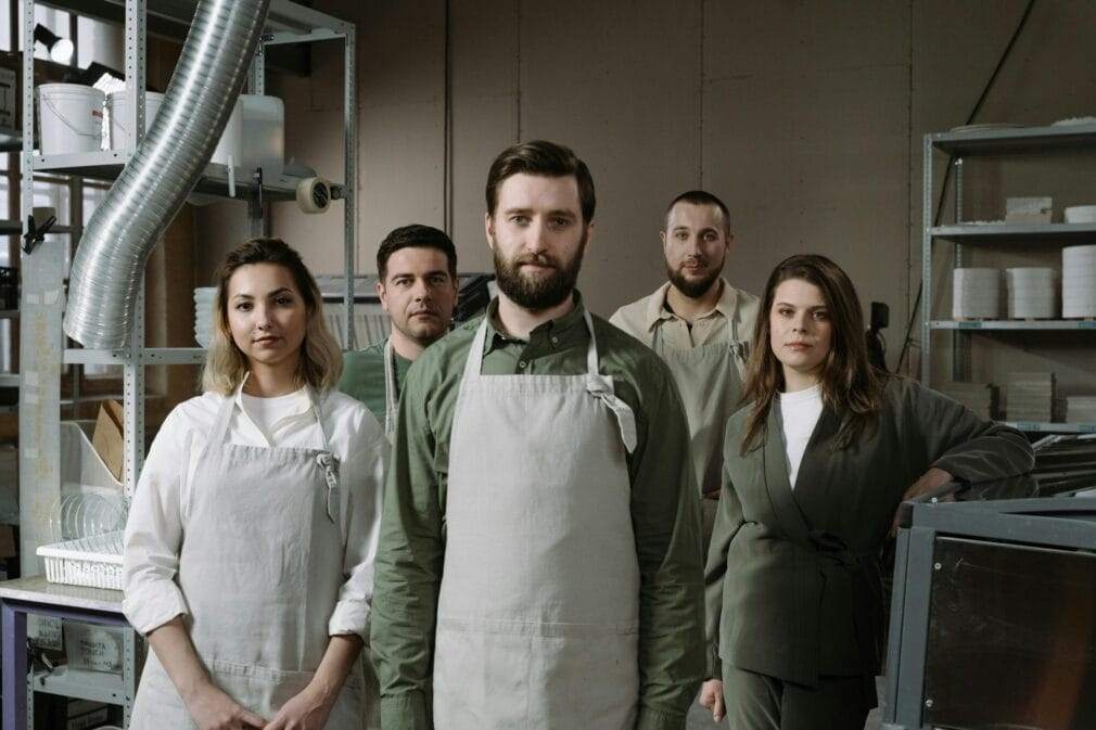 A diverse group of artisans standing together in a pottery studio, dressed in aprons.