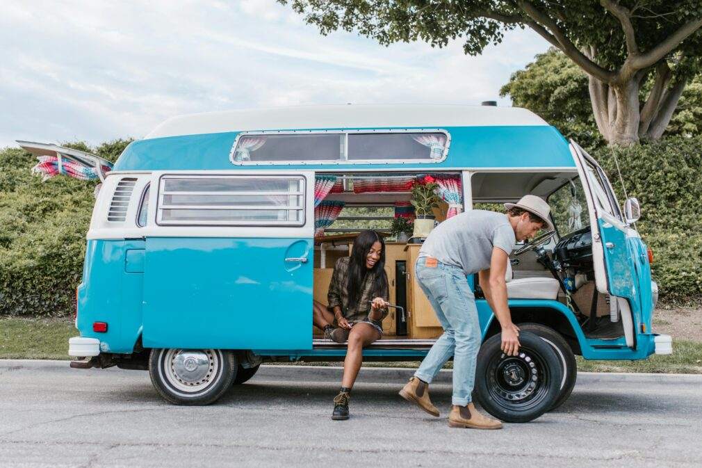 A couple enjoying a road trip, fixing a tire on their vintage Volkswagen van parked outdoors.