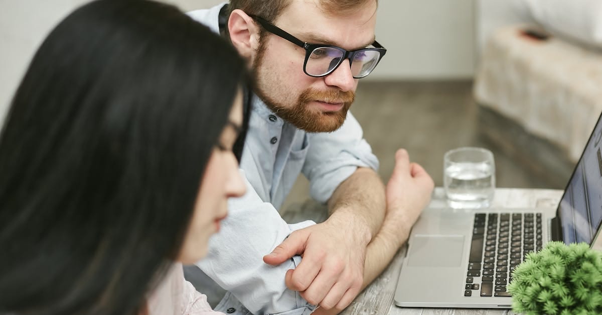 A man and woman sitting at a table reviewing documents on a laptop indoors.