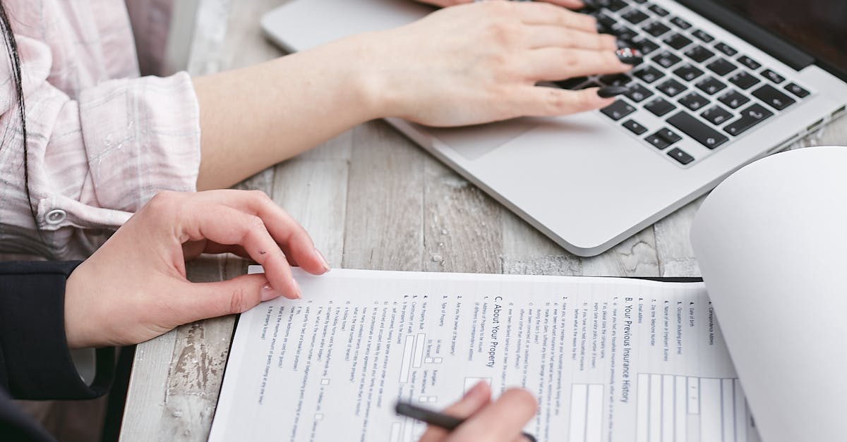 Close up of hands typing on a laptop and reviewing business documents, focused on finance and legal tasks.